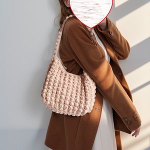 May include: A brown blazer with a pink crocheted handbag. The person is wearing a white dress underneath the blazer.