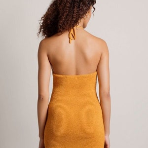 May include: A mustard yellow halter dress with a ribbed knit texture. The dress is sleeveless and has a fitted silhouette.
