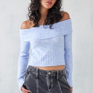 Peut inclure: Un pull bleu clair à épaules dénudées avec des manches longues et une coupe courte. Le pull est fait d'un matériau doux et duveteux.