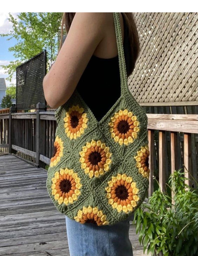 Puede incluir: Un bolso tote de crochet verde con un patr&oacute;n de girasol. El bolso tiene una correa larga y est&aacute; hecho de un hilo suave y texturizado.