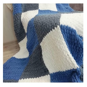 May include: A chunky knit blanket with a checkered pattern in shades of blue, gray, and white.