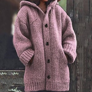 Op de afbeelding: Een lange mouwen, gekapte cardigan trui in een licht roze kleur. De trui heeft een knoopsluiting en zakken aan de zijkanten.