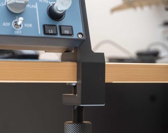 May include: A detailed shot of an aircraft instrument panel, featuring a blue control surface with buttons, dials, and a digital display. The panel is secured by a black clamp to a wooden surface. The panel has the text "WPT", "NAV", "VOR", "CSTR", "ADF", "LS", and "FD".