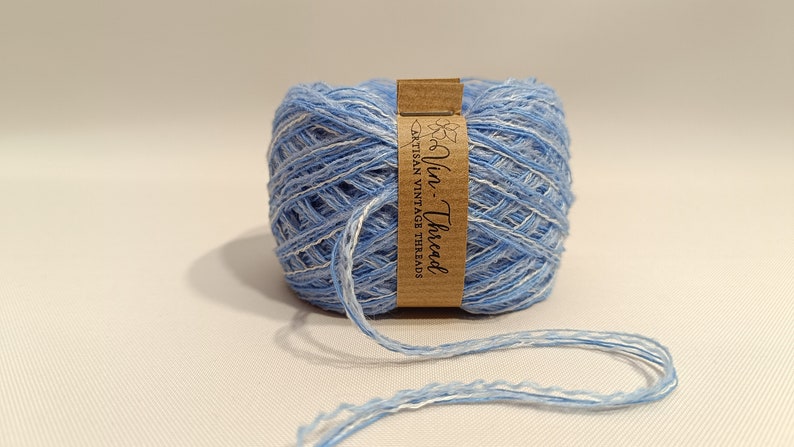 K&ouml;nnte beinhalten: Eine Spule blaues und wei&szlig;es Garn mit einem braunen Etikett, auf dem "Vin-Thread Artisan Vintage Threads" steht.