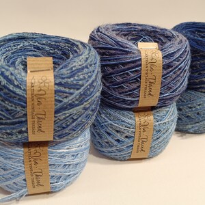 K&ouml;nnte beinhalten: Vier Kn&auml;uel blaues und graues Garn mit einem braunen Etikett mit der Aufschrift "Yarn-Thread Artisan Vintage Threads".