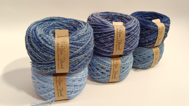 K&ouml;nnte beinhalten: Vier Kn&auml;uel blaues und graues Garn mit einem braunen Etikett mit der Aufschrift "Yarn-Thread Artisan Vintage Threads".