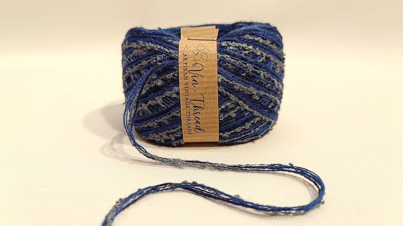 K&ouml;nnte beinhalten: Eine blaue und graue Garnrolle mit einem braunen Etikett, auf dem "Vin-Thread Artisan Vintage Threads" steht.