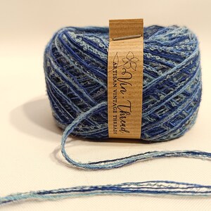 K&ouml;nnte beinhalten: Eine blaue und hellblaue Garnrolle mit einem braunen Etikett, auf dem "Vin - Thread Artisan Vintage Thread" steht.
