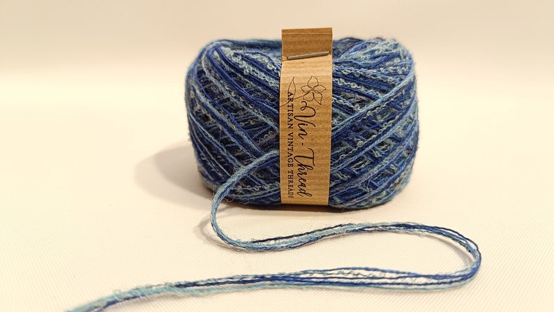 K&ouml;nnte beinhalten: Eine blaue und hellblaue Garnrolle mit einem braunen Etikett, auf dem "Vin - Thread Artisan Vintage Thread" steht.