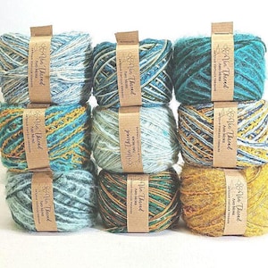Pode incluir: Nove novelos de fio colorido em tons de azul, verde-azulado e dourado. Cada novelo é embrulhado com uma faixa de papel castanho que diz "Via Thread Artisan Vintage Threads". O fio está disposto em três filas de três.