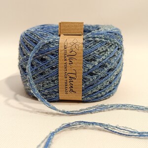 K&ouml;nnte beinhalten: Eine Spule blauen und wei&szlig;en Garns mit einem braunen Etikett, auf dem "Vin. Thread Artisan Vintage Threads" steht.