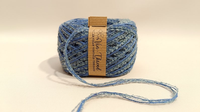 K&ouml;nnte beinhalten: Eine Spule blauen und wei&szlig;en Garns mit einem braunen Etikett, auf dem "Vin. Thread Artisan Vintage Threads" steht.