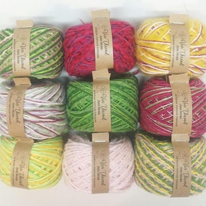 Puede incluir: Nueve madejas de hilo colorido, cada una envuelta con una banda de papel marrón que dice "Vin Thread AND MORE ARTISAN VINTAGE THREADS". Los colores del hilo incluyen verde, rosa, amarillo y rojo, con varias combinaciones de colores.