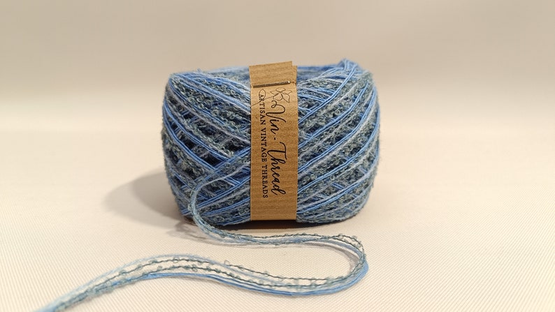 K&ouml;nnte beinhalten: Eine Spule blauen und gr&uuml;nen Garns mit einem braunen Etikett, auf dem "Via Thread Artisan Vintage Threads" steht.