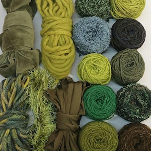 May include: Assortment of green, brown, and blue yarn, ribbon, and fabric scraps. The materials are arranged in a circle on a white surface.