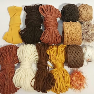 Può includere: Assortimento di filati in vari colori, tra cui marrone, bianco, arancione e giallo. Il filato è disposto in una varietà di forme e dimensioni, e alcuni dei filati sono legati insieme in fasci.