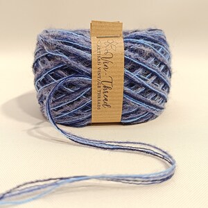 K&ouml;nnte beinhalten: Eine blaue und graue Garnrolle mit einem braunen Etikett, auf dem "Vin-Thread" und "Artisan Vintage Threads" steht.