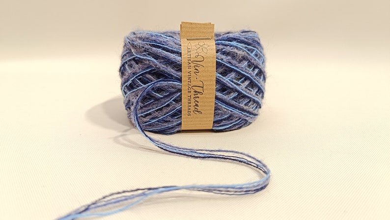 K&ouml;nnte beinhalten: Eine blaue und graue Garnrolle mit einem braunen Etikett, auf dem "Vin-Thread" und "Artisan Vintage Threads" steht.