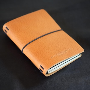 May include: A tan leather bound journal with an elastic closure and the text "Highland Leather Co." embossed on the cover.