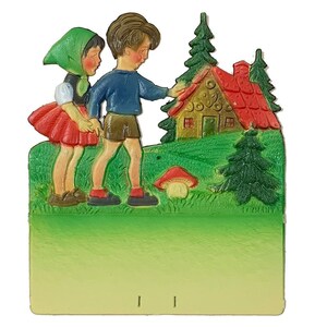May include: A vintage papercraft scene depicting two children standing in front of a gingerbread house. The house is decorated with red and white icing and has a brown roof. The children are wearing colorful clothing and are looking at the house. The scene is set in a green forest with a mushroom in the foreground.