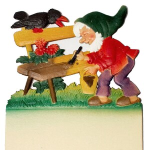 May include: A gnome with a green hat and red shirt is painting a wooden bench with a paintbrush. A black crow is perched on the bench. There are red flowers growing in the garden.