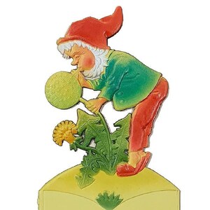 May include: A whimsical gnome figurine blowing on a dandelion with a yellow background. The gnome is wearing a red hat, green shirt, and red pants. The dandelion is green with a yellow flower.