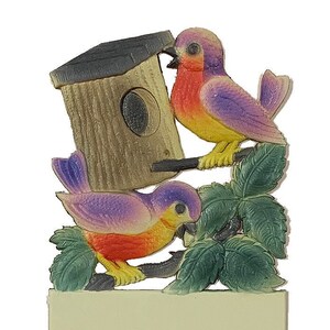 May include: A wooden birdhouse with a brown roof and a small opening for birds to enter. Two purple and yellow birds are perched on the birdhouse and a branch with green leaves.