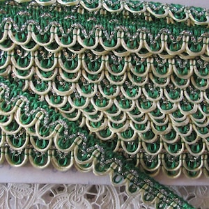May include: Green and cream trim with silver thread. The trim has a scalloped edge and is made of a woven fabric.