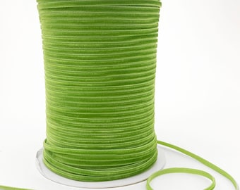 May include: A spool of bright green velvet ribbon. The ribbon is wound tightly around a white cardboard spool.