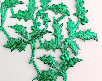 May include: A set of green metallic holly sprigs with red berries. The sprigs are made of thin, shiny metal and have a realistic appearance.