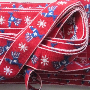 May include: Red ribbon with a repeating pattern of blue birds and white snowflakes. The ribbon has a white border and is tightly coiled, showcasing the detailed embroidery. This decorative ribbon is suitable for crafts and holiday projects.