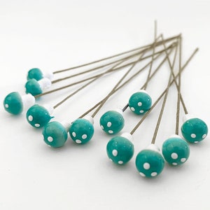 May include: A set of 12 teal blue mushroom-shaped embellishments with white polka dots, each attached to a thin brown wire stem.