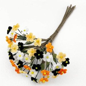 May include: A bunch of small velvet flowers in orange, white, and black colors. The flowers are attached to thin brown stems.