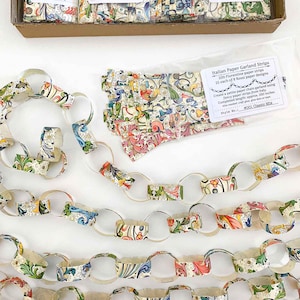 May include: Paper garland strips with colorful floral patterns. The image shows a chain of paper links and a package of strips. The text on the package says "Italian Paper Garland Strips" and "200 Florentine paper strips".