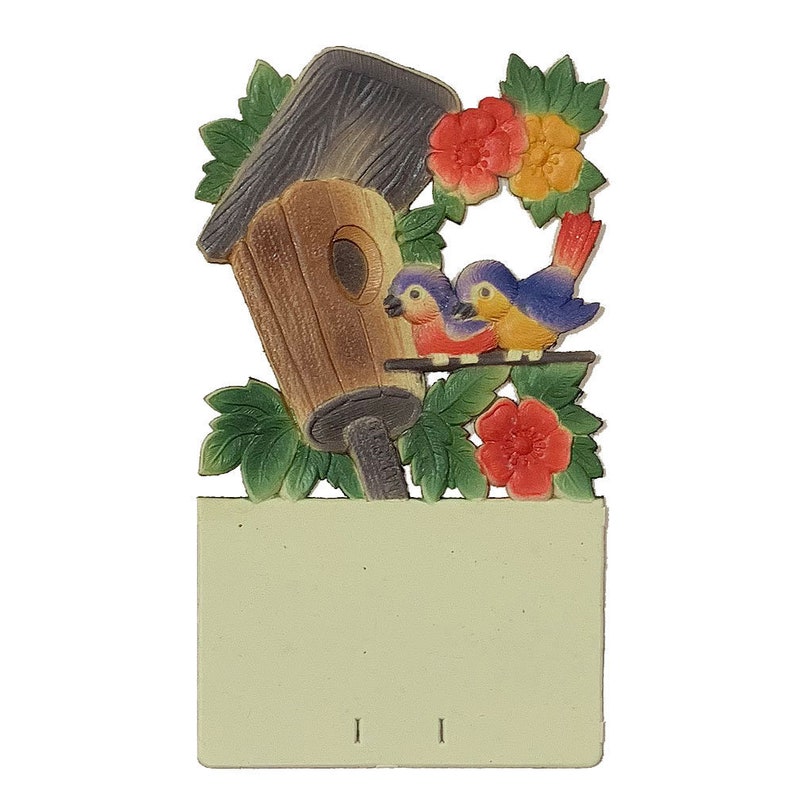 May include: A wooden birdhouse with a brown roof and a bluebird couple perched on a branch. The birdhouse is surrounded by green leaves and red flowers.