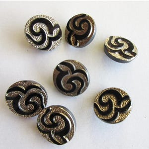 May include: Six black and silver buttons with a swirling design. The buttons are round and have a shiny finish.