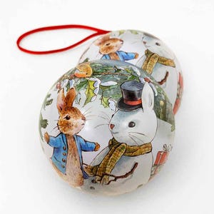 May include: Two round Christmas ornaments with a winter scene featuring a rabbit and a snowman. The ornaments are white with a glossy finish and have a red string for hanging.