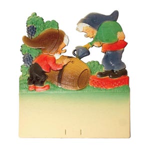 May include: A vintage, 3D, paper-mache Christmas card featuring two gnomes. One gnome is pouring water from a watering can onto a wooden barrel while the other gnome is holding the barrel. The card has a blank space for writing a message.