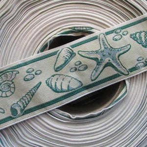 May include: A roll of beige ribbon with a green border featuring sea life designs. The ribbon showcases starfish, seashells, and small round shapes. The ribbon is rolled up, revealing the texture and pattern.