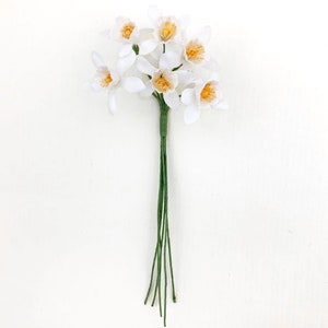 May include: A bunch of white paper daffodils with yellow centers. The stems are green and tied together.