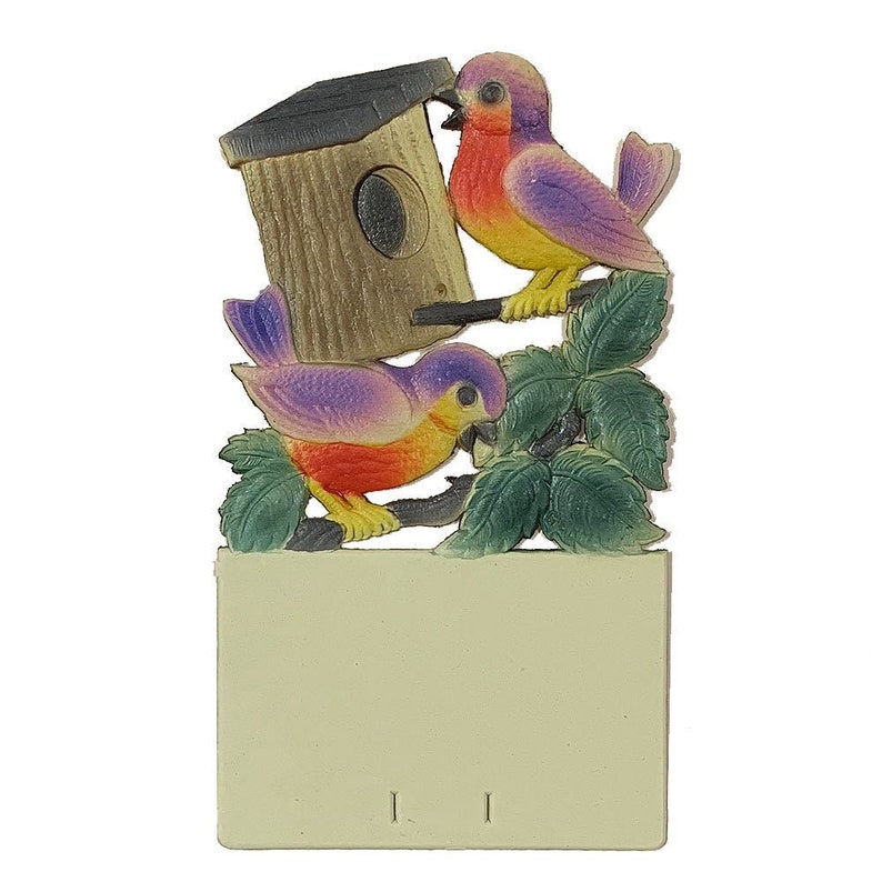 May include: A wooden birdhouse with a brown roof and a small opening for birds to enter. Two purple and yellow birds are perched on the birdhouse and a branch with green leaves.