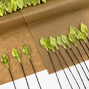 May include: A collection of green velvet leaves on brown wire stems. The leaves are arranged in rows on a brown paper surface.