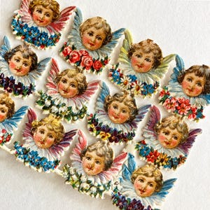 May include: A collection of vintage-style angel die-cuts. Each angel has a cherubic face, adorned with a ruffled collar and floral accents in shades of blue, red, and white. The wings are light blue and pink.