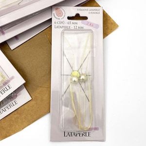 May include: A package of two silver-colored metal beads with gold-colored wire loops. The package is labeled "LATAPERLE" and includes the text "6 CÍPU - 65 MM" and "LATAPERLE - 12 MM".