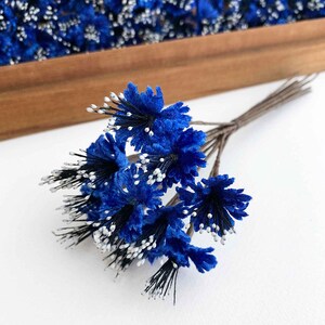 May include: A bouquet of blue paper flowers with white centers and black stems. The flowers are arranged in a cluster and are ready to be used for crafting or decorating.