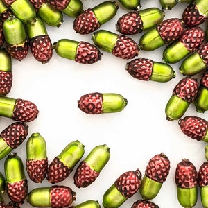 May include: A collection of green and red acorn-shaped glass beads. The beads are arranged in a circle on a white background.