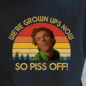 May include: Black t-shirt with a retro graphic featuring a man's face and the text "WE'RE GROWN UPS NOW SO PISS OFF!". The graphic has a sunset design with trees.