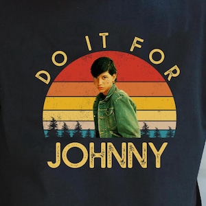 May include: Black t-shirt with a retro sunset graphic featuring a person and the text "DO IT FOR JOHNNY" in yellow. The graphic has a vintage aesthetic, with a person in a green jacket.