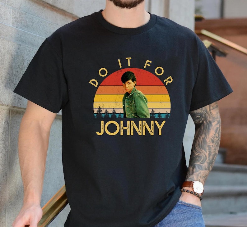 May include: Black t-shirt with a retro sunset graphic featuring a person and the text "DO IT FOR JOHNNY" in yellow. The graphic has a vintage aesthetic, with a person in a green jacket.