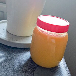 May include: A clear glass jar with a red lid filled with a bright orange liquid. The jar is sitting on a grey and black patterned surface.